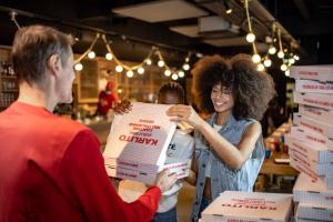 a woman is handing a man a stack of pizza boxes at MOB HOTEL Paris Les Puces in Saint-Ouen