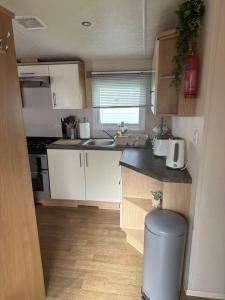 a small kitchen with white cabinets and a trash can at Phoenix caravan hire, Trecco bay in Porthcawl