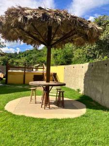 a picnic table with a straw umbrella in the grass at Recanto da Caluninha in Esmeraldas