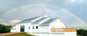 a white barn with a rainbow in the sky at New Field Farm at Timber Ridge in Lexington