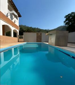 a swimming pool with blue water in front of a house at Refúgio na natureza com piscina e churrasqueira in Pedro de Toledo