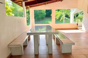 a glass table and benches in a room with windows at Refúgio na natureza com piscina e churrasqueira in Pedro de Toledo