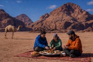 three men eating food in the desert with a camel in the background at Wadi rum bubble camp in Wadi Musa