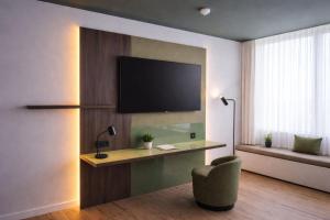 a living room with a television on a wall with a chair at Holiday Inn Cottbus by IHG in Cottbus
