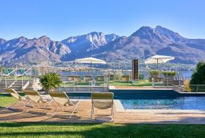 a group of chairs sitting next to a pool with mountains at Bellagio Village - Holiday Apartments by the Lake - Seasonal Warm Pool and Sauna in Oliveto Lario