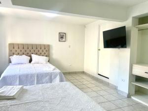 a white bedroom with a bed and a flat screen tv at Casa 11 Centrica 3 camas queen in Hermosillo