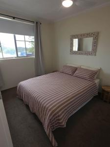 a bedroom with a bed with a striped blanket and a mirror at Crystal Waters 7 Ocean Corridor Views, Restaurants, Town Centre in Forster
