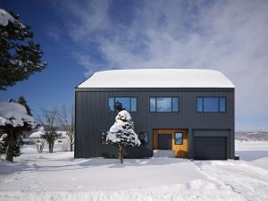 a black house in the snow with a tree at Villa Matsu by H2 Life in Nakafurano