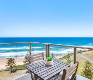 a wooden table with a potted plant on a balcony overlooking the beach at Seaside Luxe - L8 - Local Eats, Walks, Swims, CBD in Newcastle