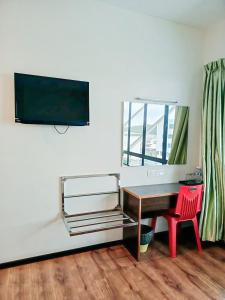 a desk with a television on a wall with a red chair at New Palace Inn in Miri