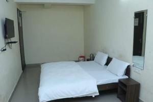 a bedroom with a bed with white sheets and a mirror at The Gopi Dham Hotel in Haridwār