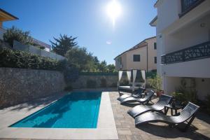 a swimming pool with two lounge chairs next to a building at Apartments Flowers - Heated Pool Near Beach in Krk
