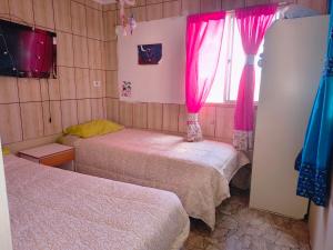 two beds in a room with pink curtains and a window at Casona Mamalluca in El Durazno