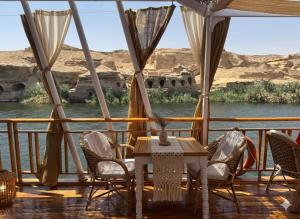 a table and chairs on a deck with a view of a river at Amber Dahabiya in Luxor