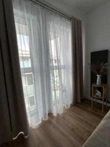 a bedroom with white curtains and a wooden floor at Apartament Parkowa-prywatny parking in Olecko