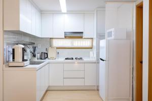 a white kitchen with white cabinets and a refrigerator at Sai-gil stay in Busan