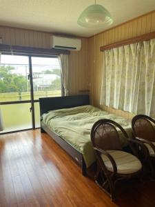 a bedroom with a bed and two chairs and a window at Adventure Hostel う島や in Iriomote