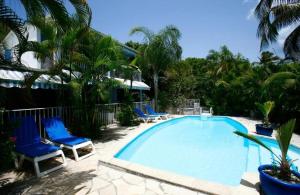 a swimming pool with blue chairs and palm trees at Studio accès piscine, plage à 50m in Le Gosier