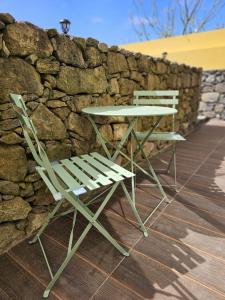 a table and two chairs next to a stone wall at The Yellow Cottage in Lomba de São Pedro