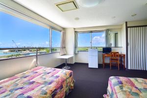 a room with two beds and a desk and windows at Hotel South Island in Miyako Island