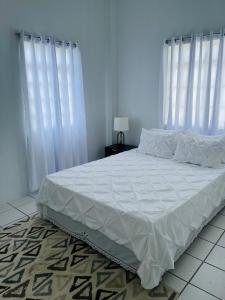 a bedroom with a bed with white sheets and white curtains at Lyn Tropical Getaway in Port-of-Spain