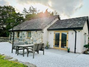 a stone cottage with a table and benches in front of it at Y Beudy Bach in Llanfor