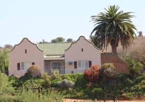 a house with a palm tree in a garden at Grysbok Self Catering Accommodation in Oudtshoorn