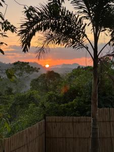 a sunset in the mountains with a fence and a palm tree at Vista Cadlao in El Nido
