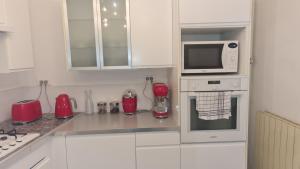 a kitchen with white cabinets and a microwave and red appliances at Appartement Duplex nimes centre160m2 climatisation 3 chambres avec parking in Nîmes