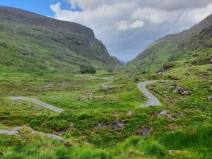 a winding road in a green mountain valley at An Cnocan in Sneem