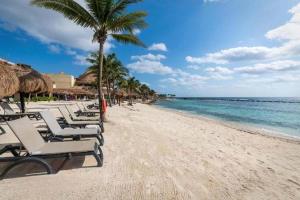 a beach with chairs and palm trees and the ocean at Estudio en Puerto Aventuras, Condominio con Alberca # 202 in Puerto Aventuras +8 photos