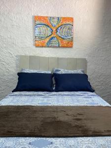 a bed with blue pillows and a painting above it at Suítes Sabor e Mar in Angra dos Reis