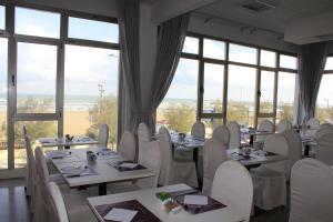 un restaurant avec des tables blanches, des chaises et des fenêtres dans l'établissement Hotel Universal, à Senigallia