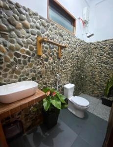 a bathroom with a sink and a toilet and a stone wall at SumateraTrekingOrangutanPatrol in Bukit Lawang