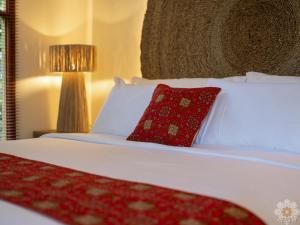 a white bed with a red pillow and a lamp at Sananda Aryani in Lovina