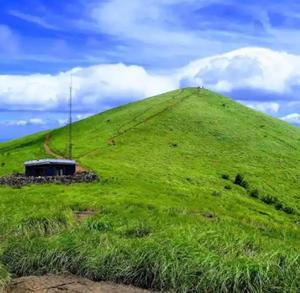 a green hill with a building on top of it at Sree durga Villa Homestay in Kodoth