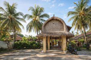 a building with a thatch roof and palm trees at GGuesthouse in Kuta Lombok