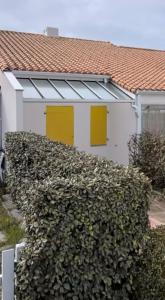 a white house with yellow doors and a hedge at Maisonnette de Plage in Saint-Hilaire-de-Riez