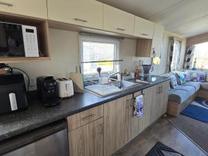 a kitchen with a sink and a living room at Seaside Caravan Home in Reighton