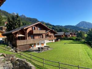 a large wooden house with a green field in front at Chalet Le Murier in Leysin