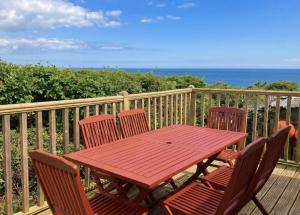 a red table and chairs on a deck with the ocean at Sunset Bay Aberaeron in Aberaeron