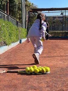 a woman running past a pile of tennis balls on a court at MSC Sport Campus in Marrakesh