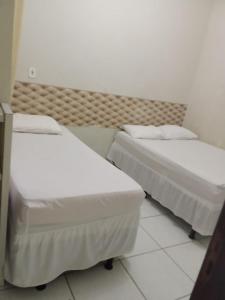 two beds in a hotel room with white sheets at Hotel São Jorge in Brumado