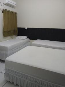 two beds in a room with white sheets at Hotel São Jorge in Brumado