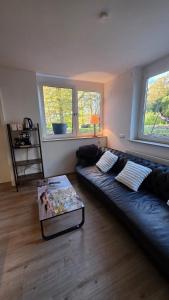 a living room with a black leather couch and two windows at Moderne 3-Zimmer-Wohnung mit separatem Eingang in Donauwörth