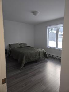 a white bedroom with a bed and a window at Appartement de 2 chambre à la baie in Saguenay