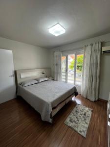 a bedroom with a bed and a large window at Casa com churrasqueira e ar para até 8 pessoas in Guabiruba