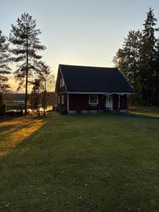 a red barn with a black roof on a grass field at Åker Lilläng Strandstugan in Åker +4 photos