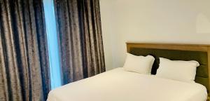 a bed with white sheets and pillows next to a window at 7th Heaven luxury Apartment in Gaborone +11 photos