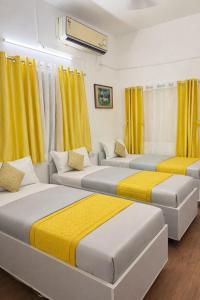 three beds in a room with yellow curtains at Elite Hostel- SB Road Pune in Pune